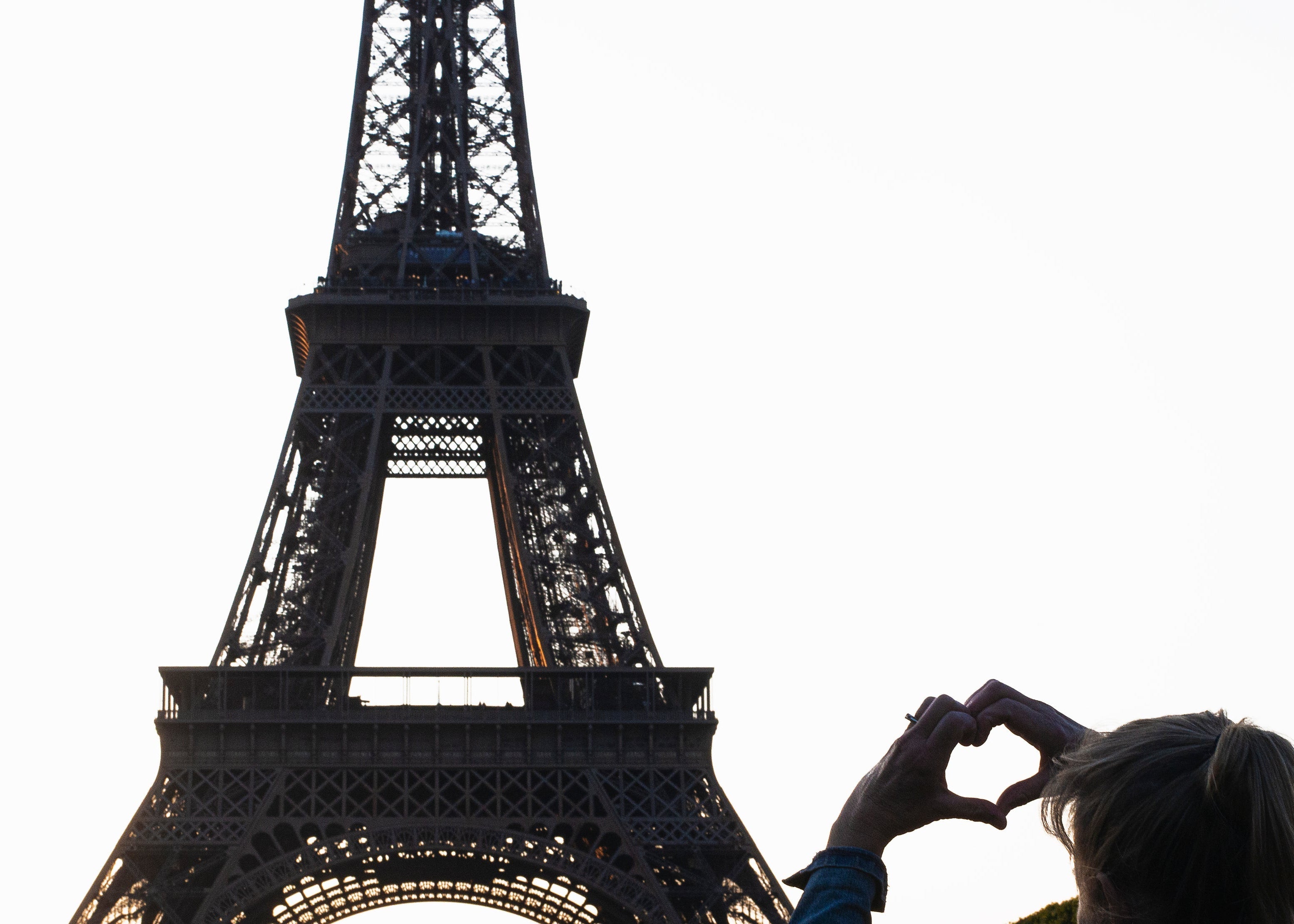 Silhouette of a person making a heart shape with their hands in front of the Eiffel Tower